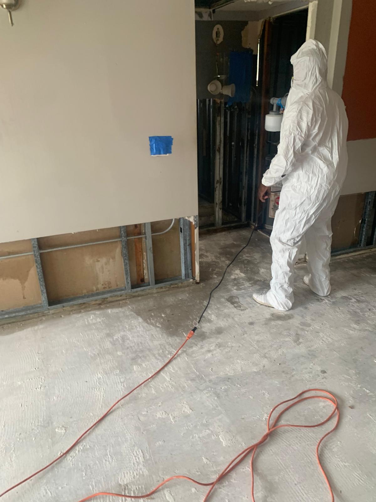 Restoration technician in protective clothing treating the interior walls of a property